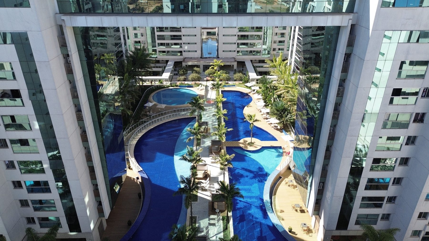 Vista aérea do conjunto de piscinas do Prime Residence, entre as torres, com deck e área verde